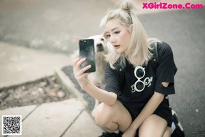 A woman sitting on top of a wooden post looking at her phone.