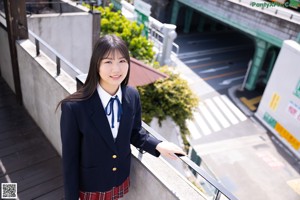 A young woman in a school uniform leaning against a wall.