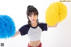 A woman in red shorts and a white shirt leaning against a wall.