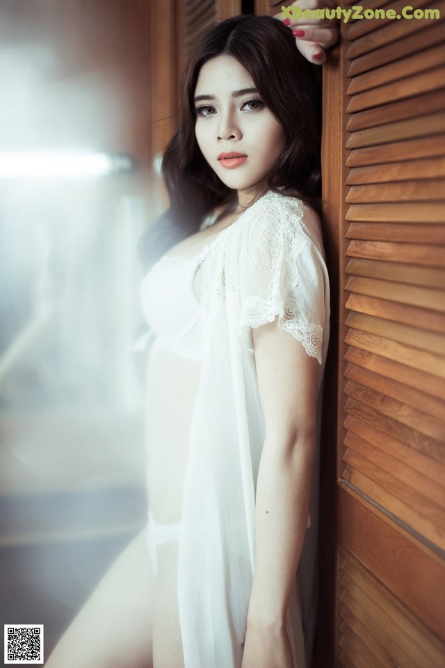 A woman in a white lingerie leaning against a wooden door.