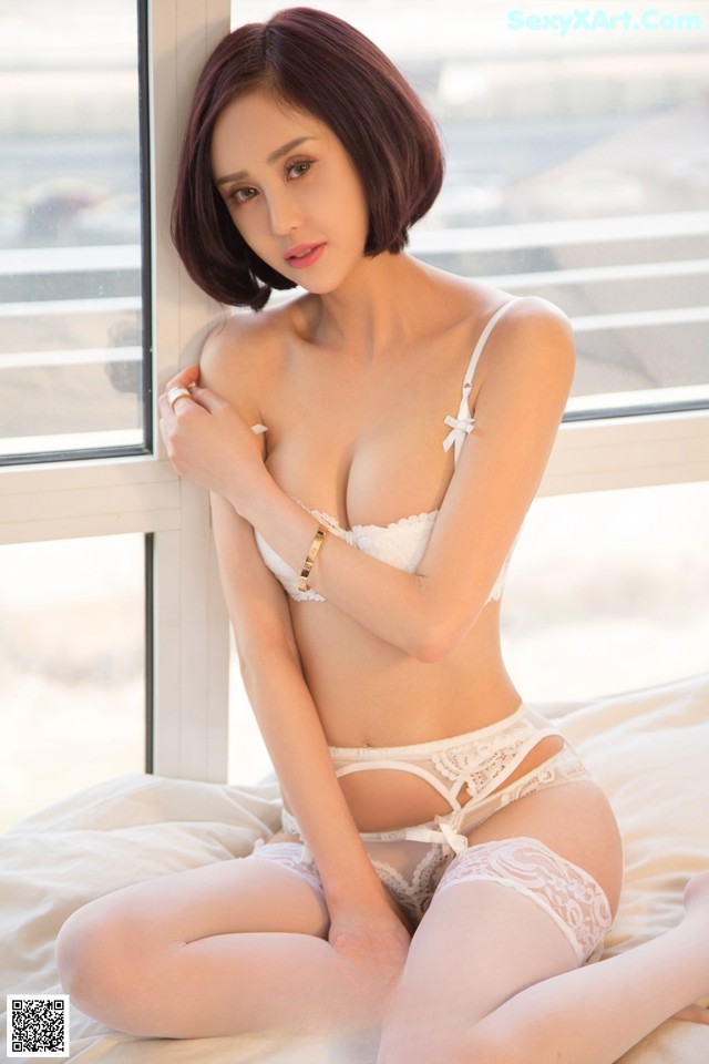 A woman in a white lingerie sitting on a bed.