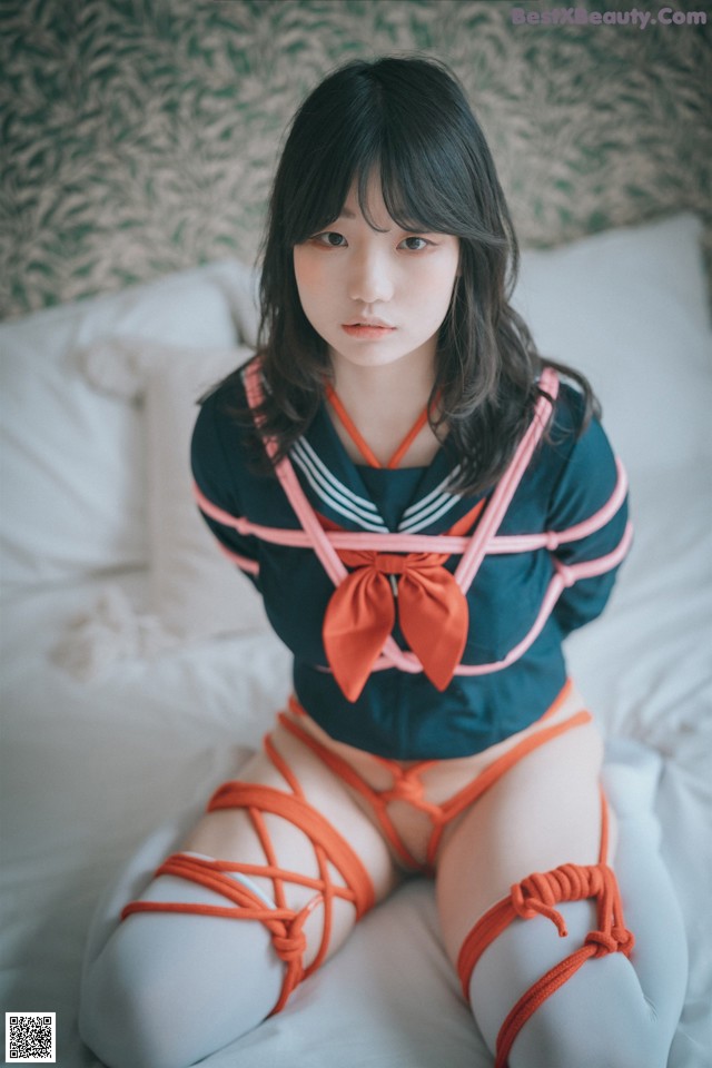 A woman in a sailor outfit sitting on a bed.