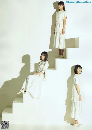 A woman in a white dress sitting on a white wall.