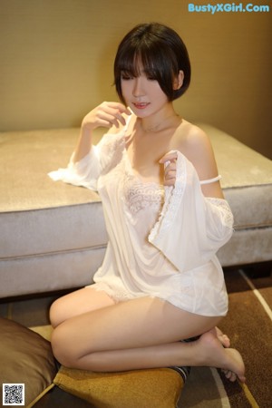 A woman in a white dress sitting on a bed.