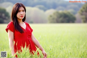 A woman in a red dress leaning against a wall.