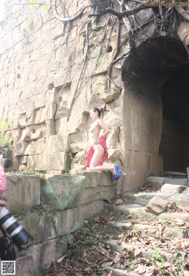 A woman in a red dress is standing on a stone wall.