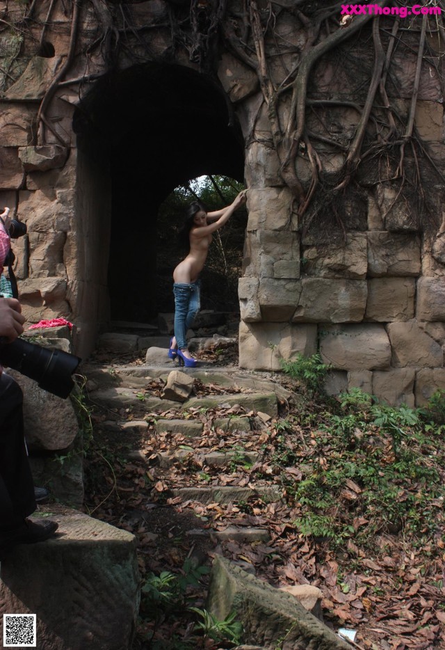 A naked woman standing in the middle of a stone tunnel.