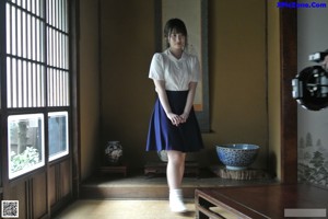 A woman in a blue dress leaning against a wall.