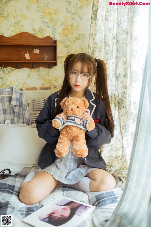 A girl sitting on a bed holding a teddy bear.