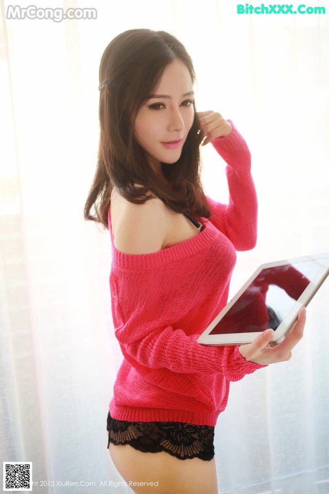 A woman in a pink sweater holding a tablet computer.